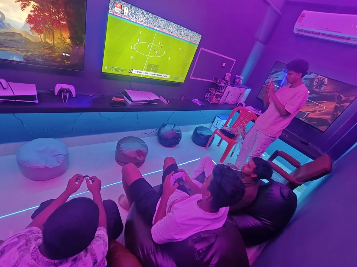 Group of friends playing an EA Sports FC football match on a big screen with bean bags under neon lighting