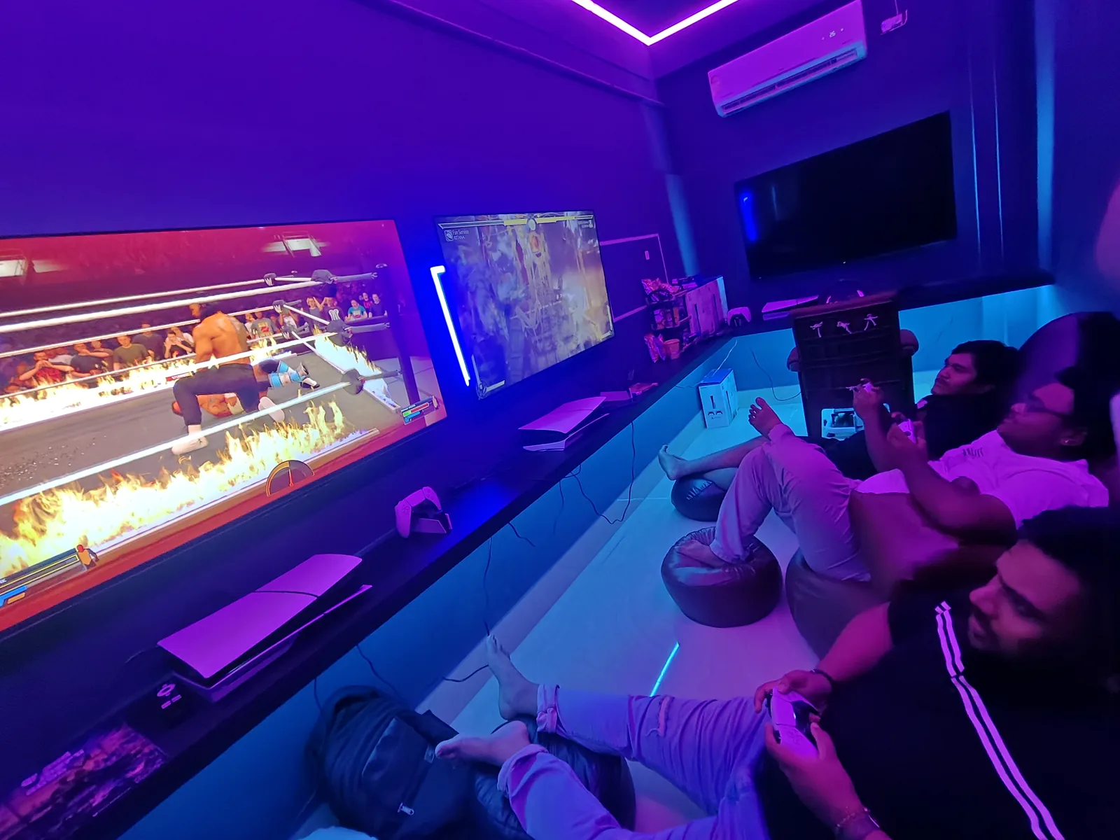 Players watching an intense WWE wrestling match with a flaming ring and a fighting game on a second screen